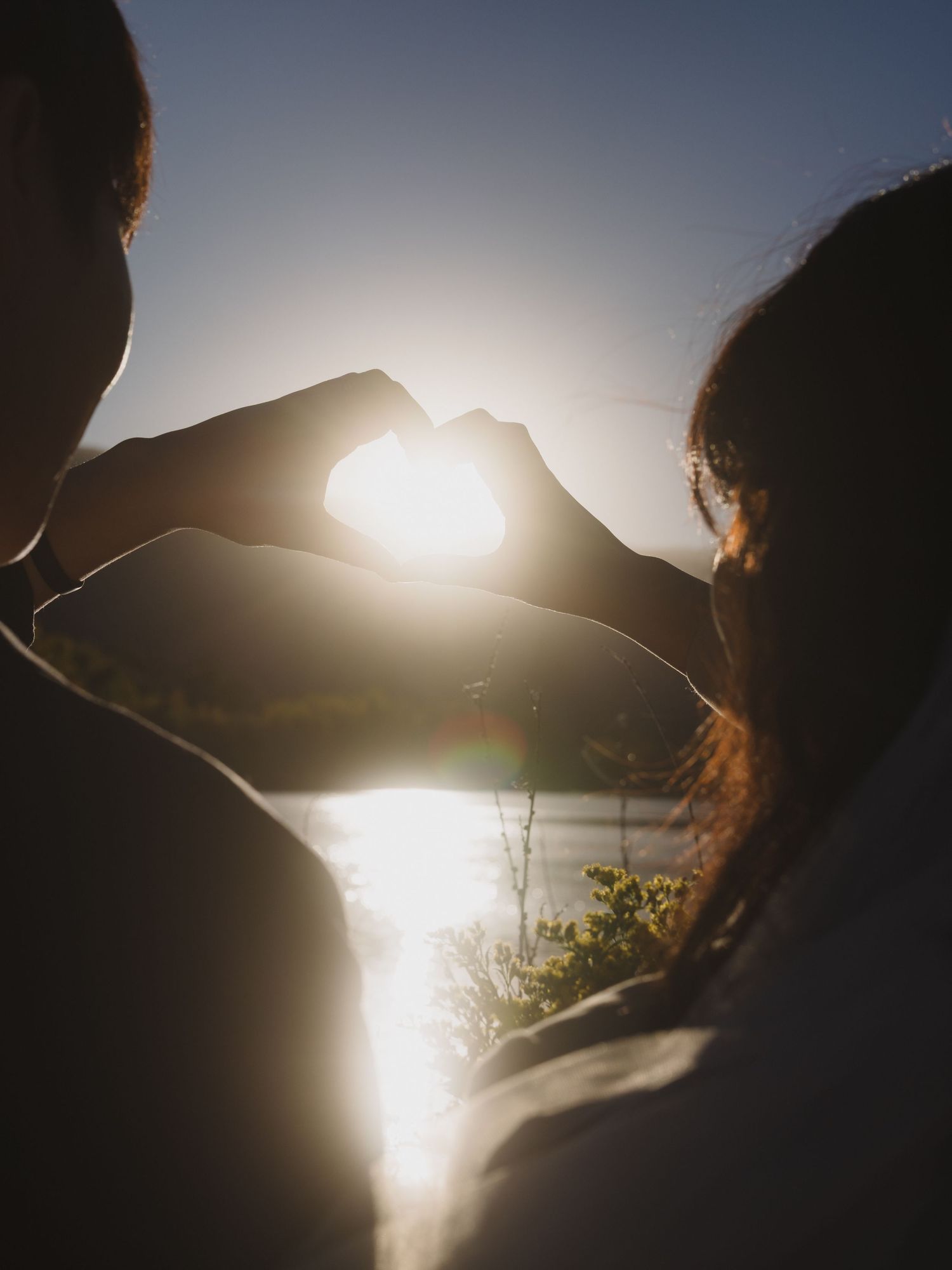 A couple in formal attire shares a joyful moment outdoors with yellow flowers against a bright blue sky.