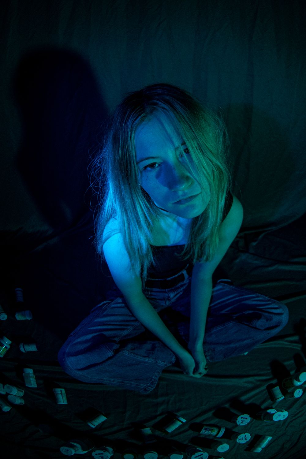 A person in dark lighting crawls on the ground surrounded by scattered playing cards with blue lighting effects.
