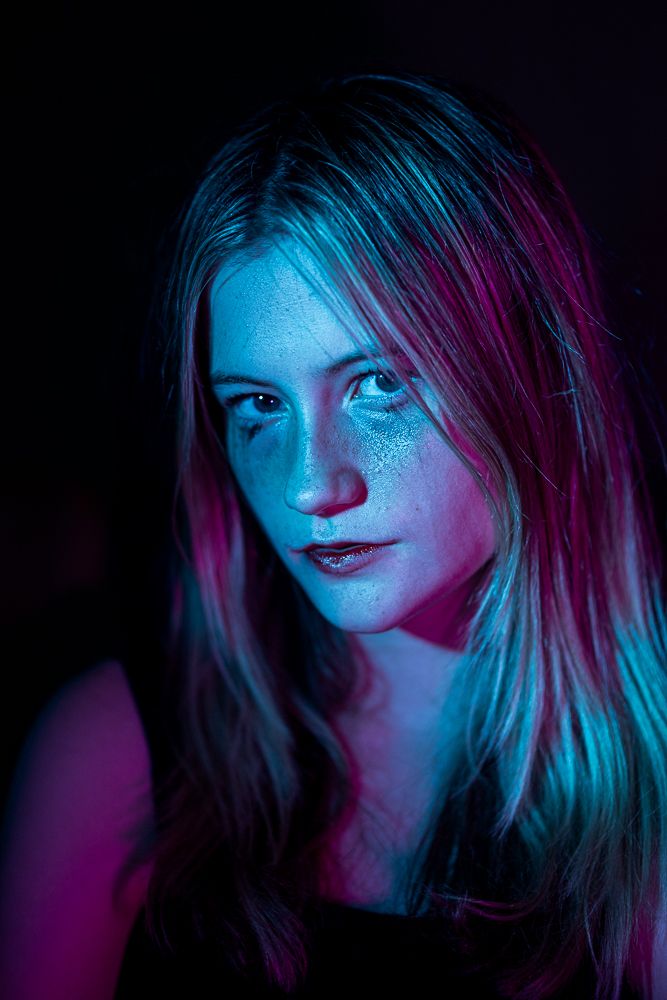 Artistic portrait with neon blue and pink lighting creating ethereal mood against dark background.