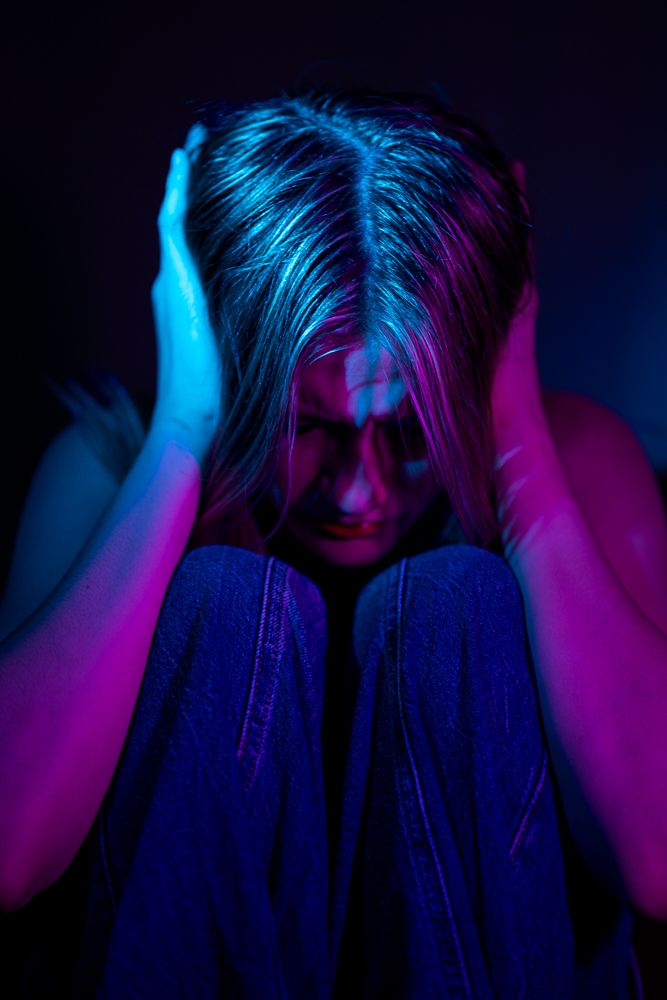 Person in dark room lit by neon blue and pink lights clutches their head in a series of dramatic poses.
