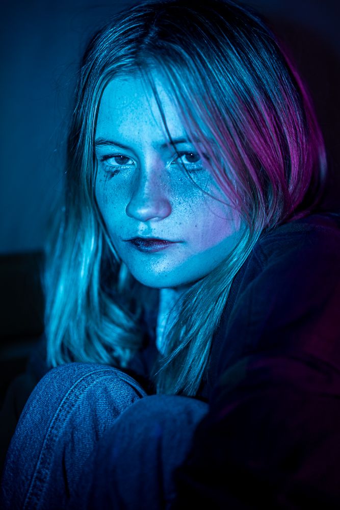 Dramatic portrait with blue and magenta lighting highlighting freckles and intense gaze.