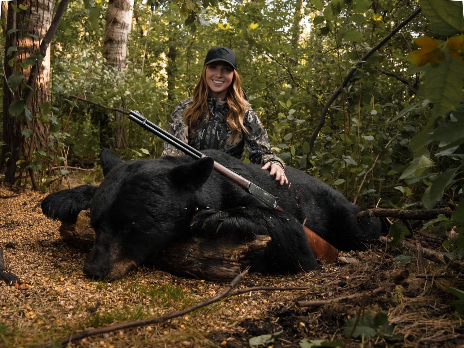 Hunter with rifle resting beside harvested black bear in autumn forest setting.