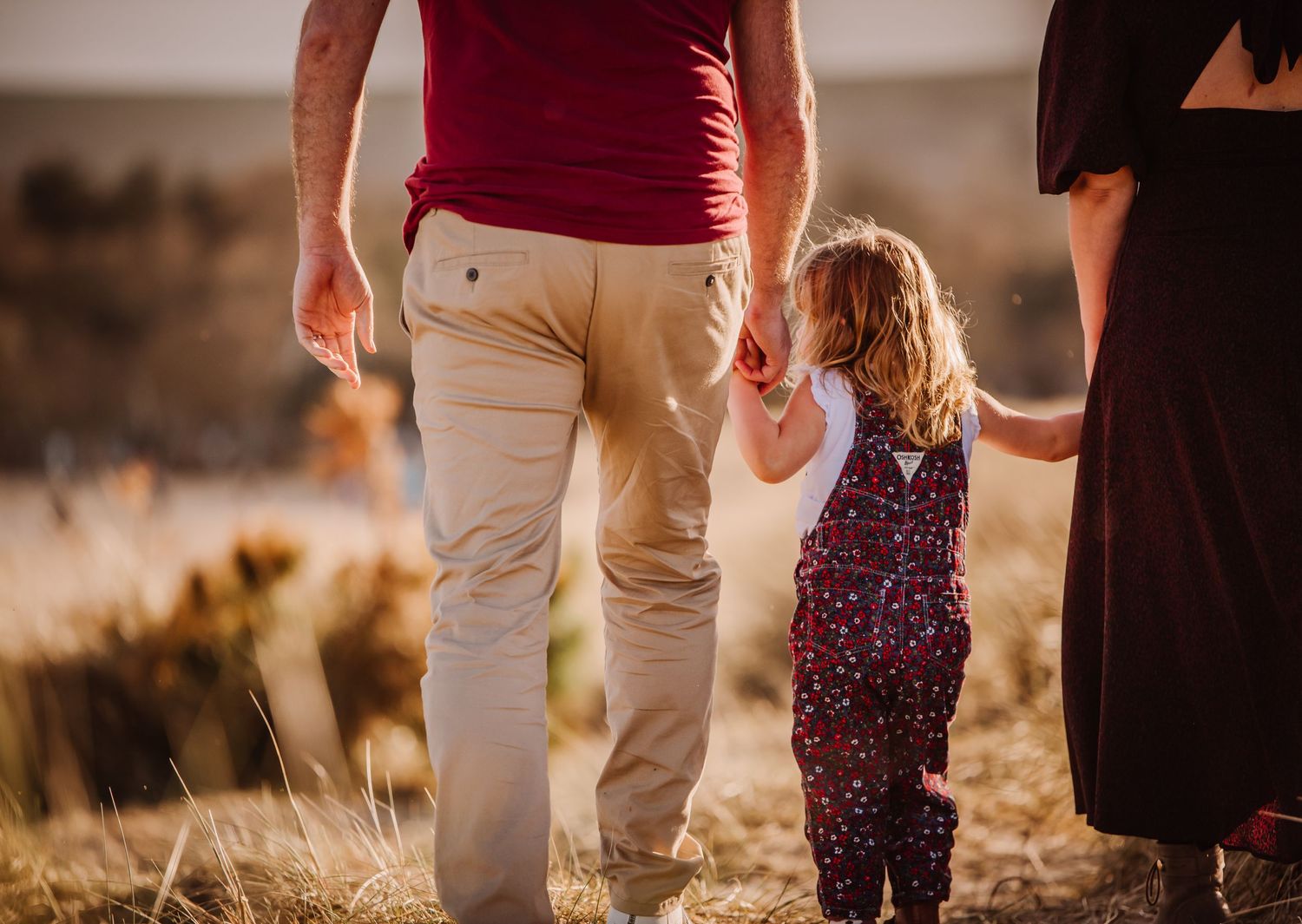 Father and his young daughter holding hands on the sand dunes at Studland, Dorset. There is a golden glow. Dorset Photographer