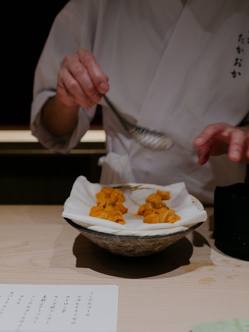 Orange uni being prepared and plated by a chef in traditional uniform.