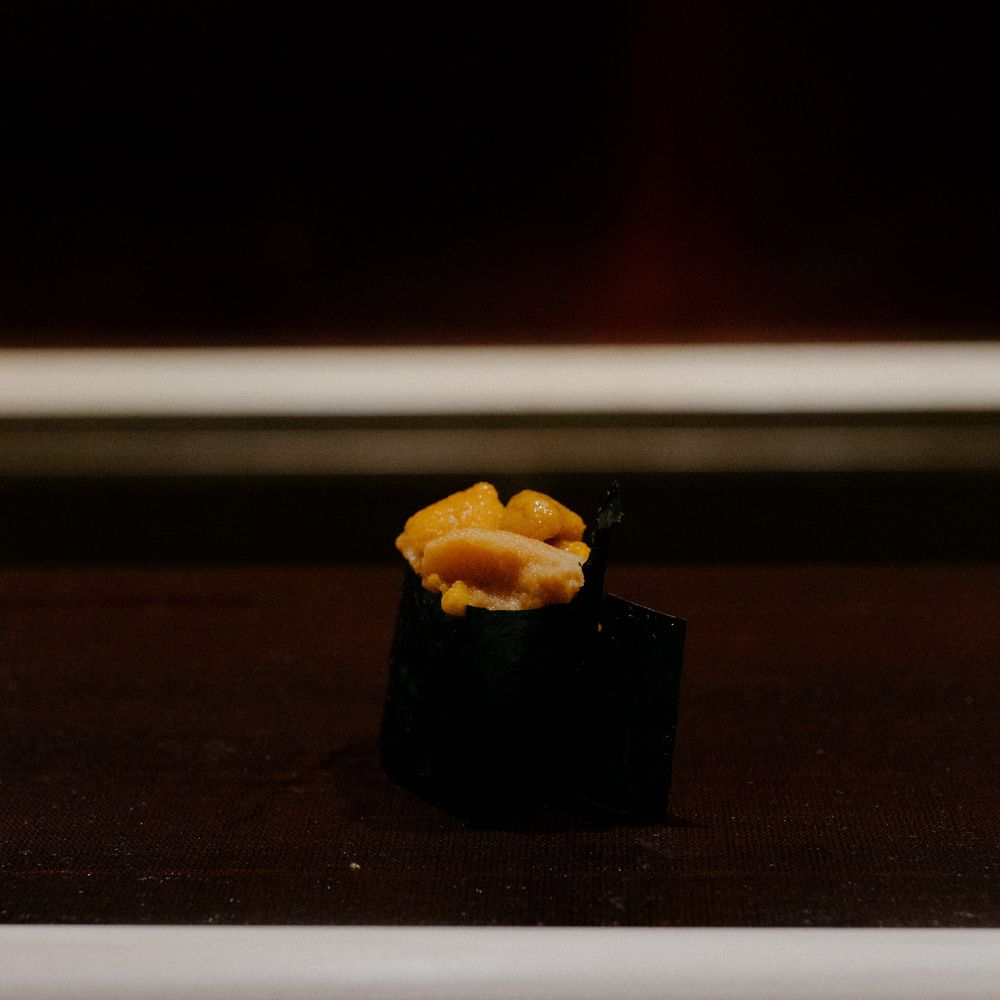 A single piece of bright orange uni served on a black pedestal.