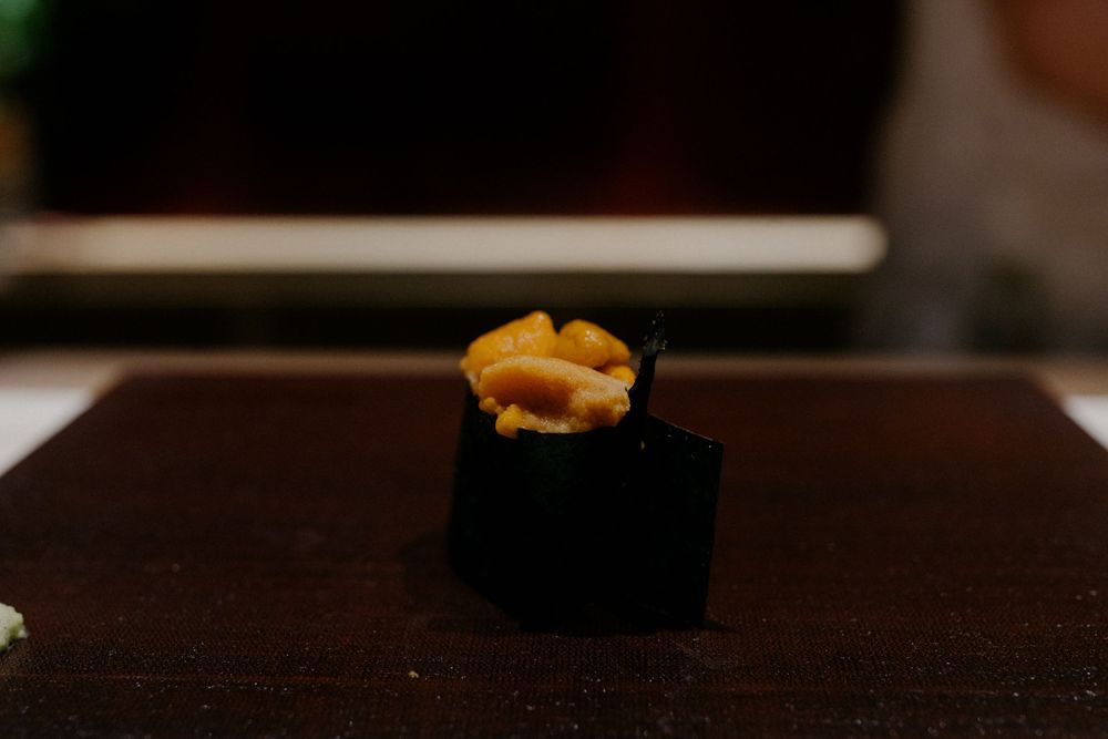 Close-up of a piece of uni sushi with orange sea urchin roe on top of dark nori wrapper.