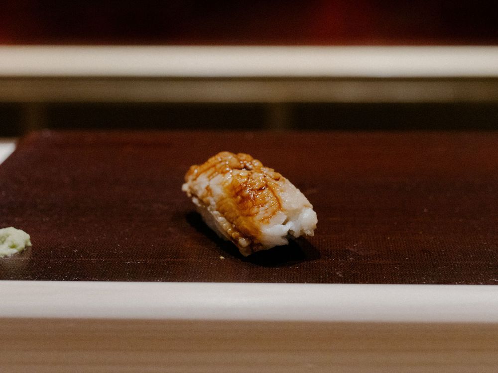 Torched nigiri sushi piece with glazed topping on a dark wooden surface.