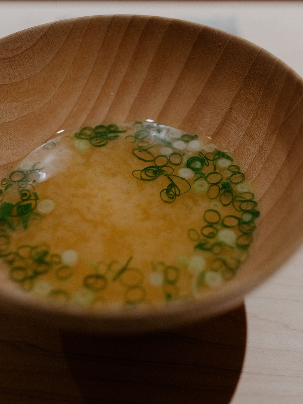 Clear miso soup in wooden bowl garnished with thin sliced green onions.