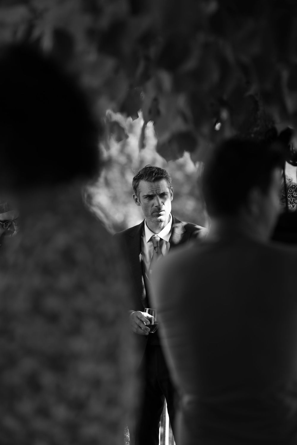 Artistic black and white photo through crowd showing figure in suit against smoky background.