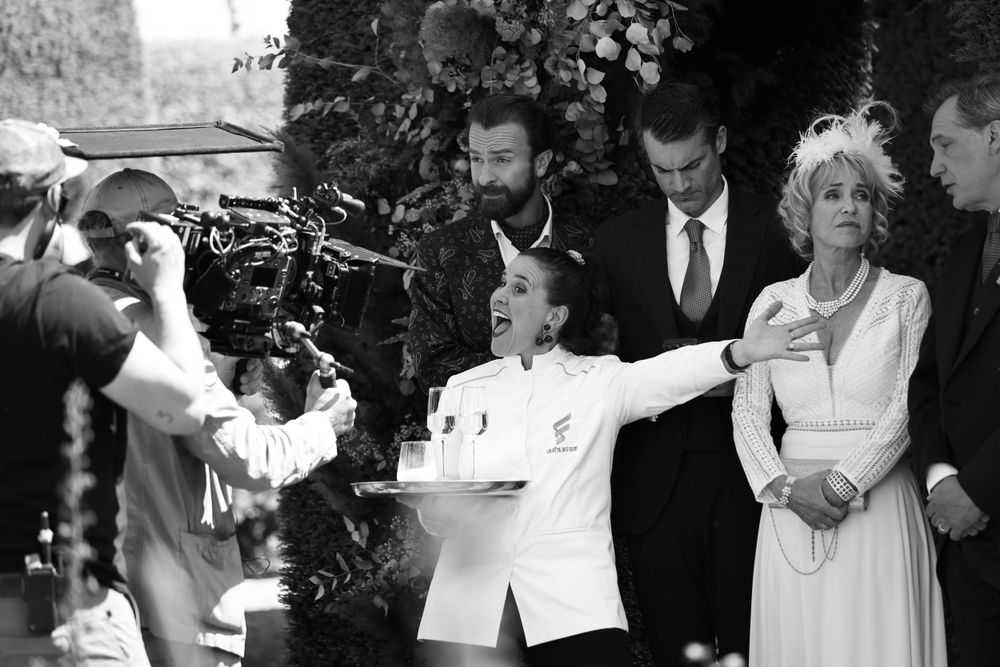 Black and white behind-the-scenes photo of film crew directing a formal scene with camera equipment.