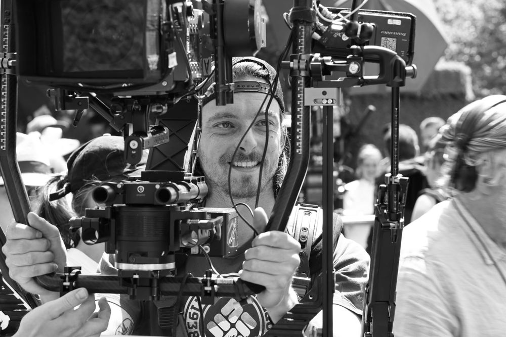Black and white image of camera operator working with professional filming equipment on set.