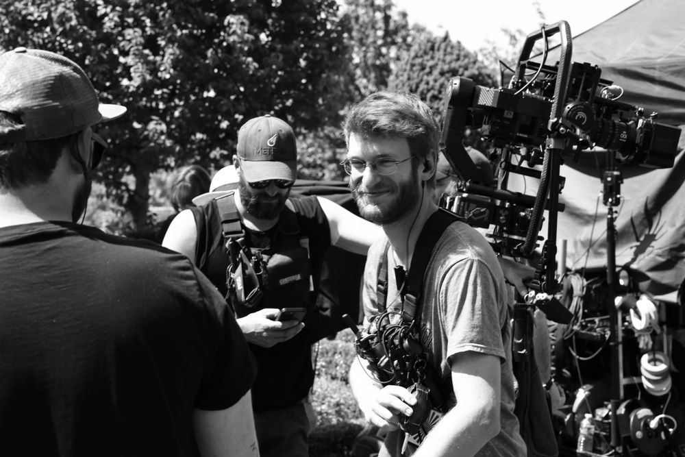 Black and white behind-the-scenes photo of film crew members with camera equipment outdoors.
