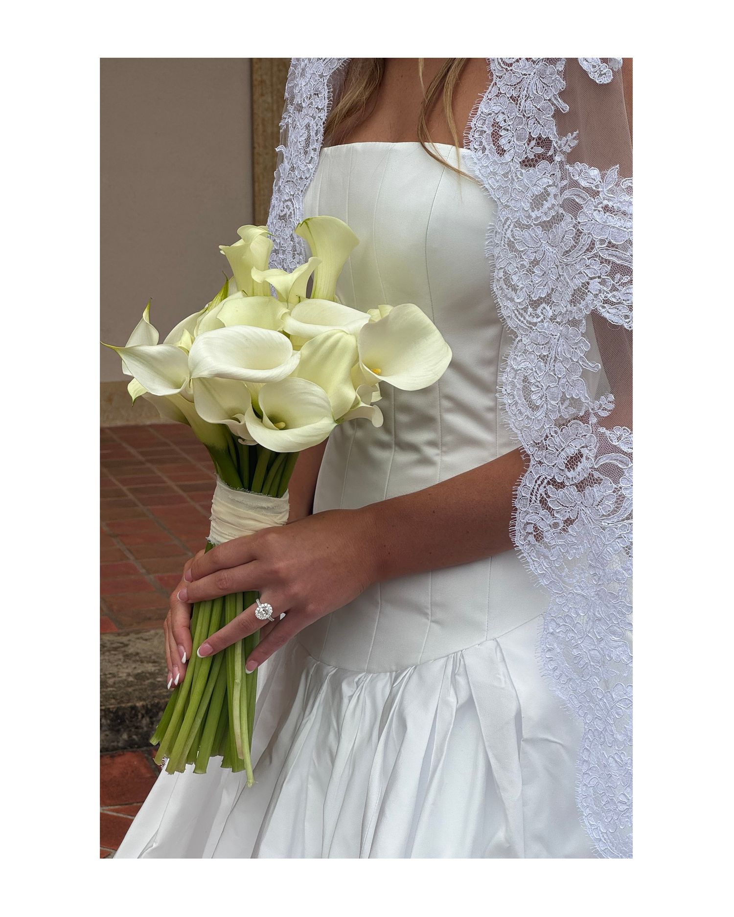 Wedding dress detail showcasing delicate lace veil and white calla lily bouquet held by bride.