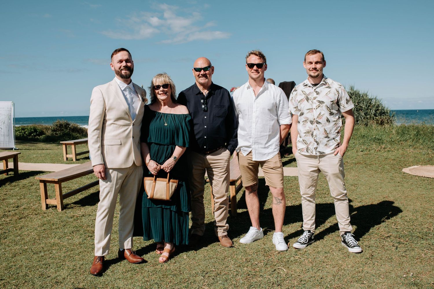 Small group posed for photo on grass with ocean view in background.