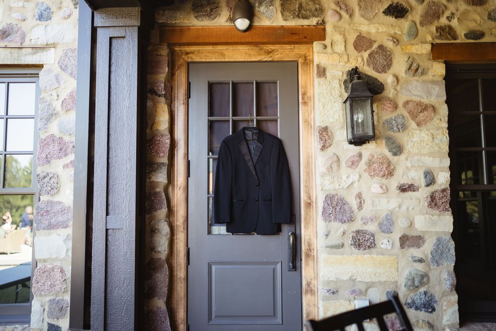 A black suit jacket hangs on a wooden door against a rustic stone wall exterior.