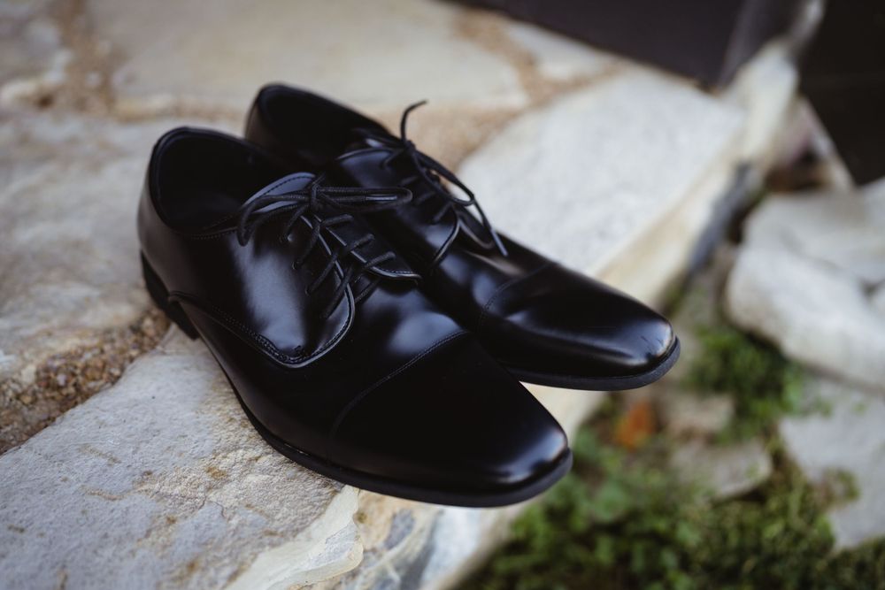 Shiny black formal dress shoes photographed on stone surface.