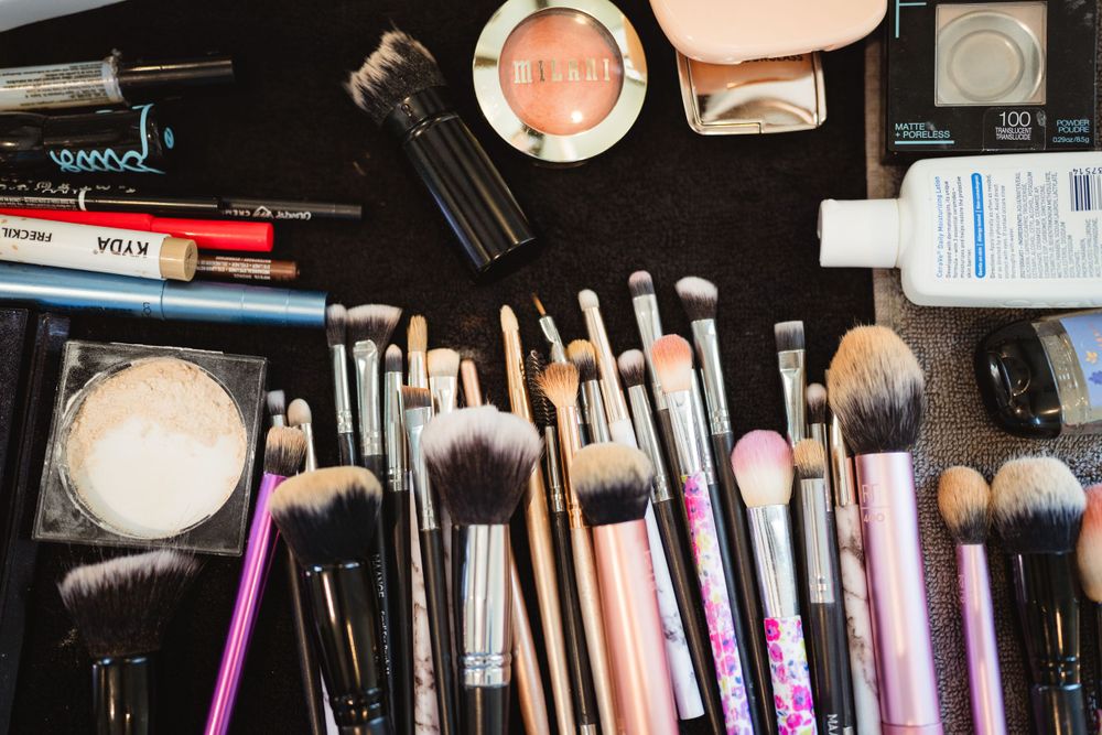 Collection of makeup brushes and cosmetic products arranged on dark surface.