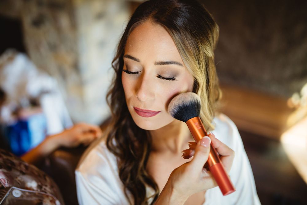 Bride getting makeup applied with a brush during wedding preparations.
