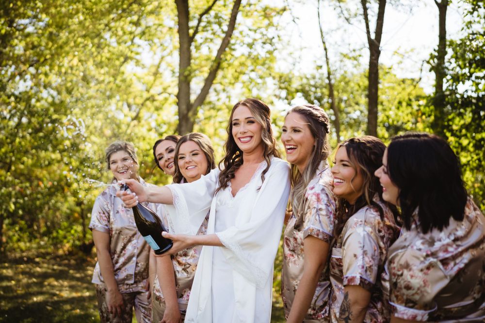 Bridal party in matching floral robes laughing together outdoors in natural lighting.