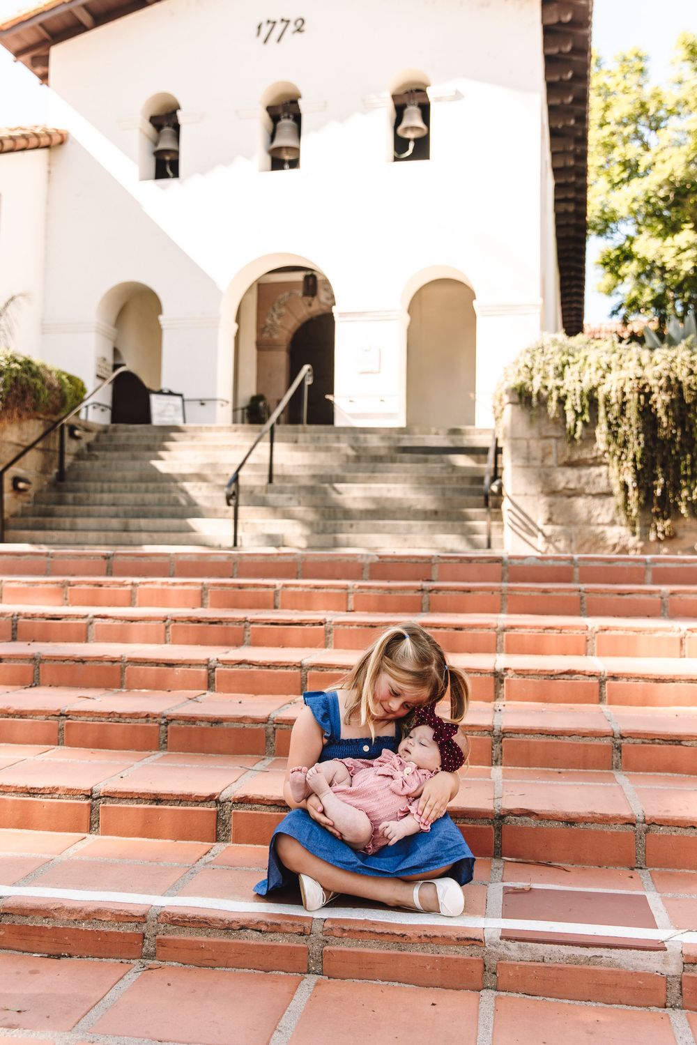 Young girl holding a newborn baby on brick steps outside a historic building.