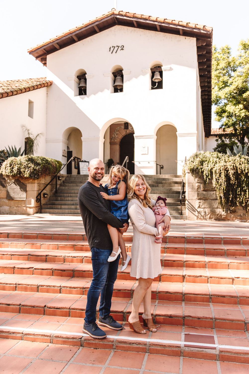 Smiling family with two young children outside a historic 1772 white church.