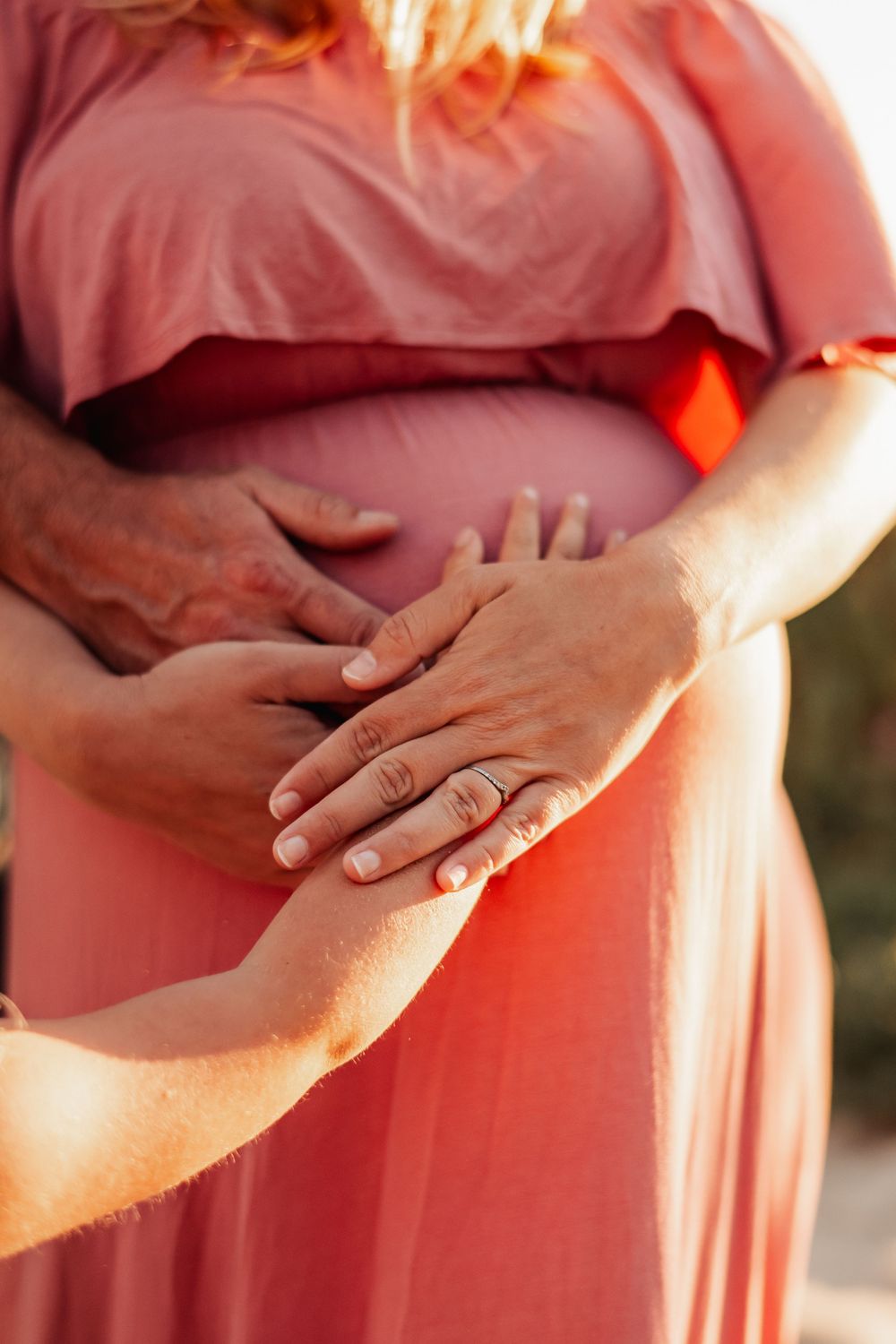 Close-up of couple's hands resting on pregnant woman's belly in pink dress.