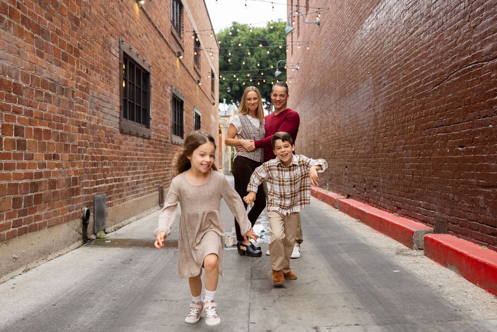 Happy family with two children running and laughing together in a brick-lined urban alleyway.