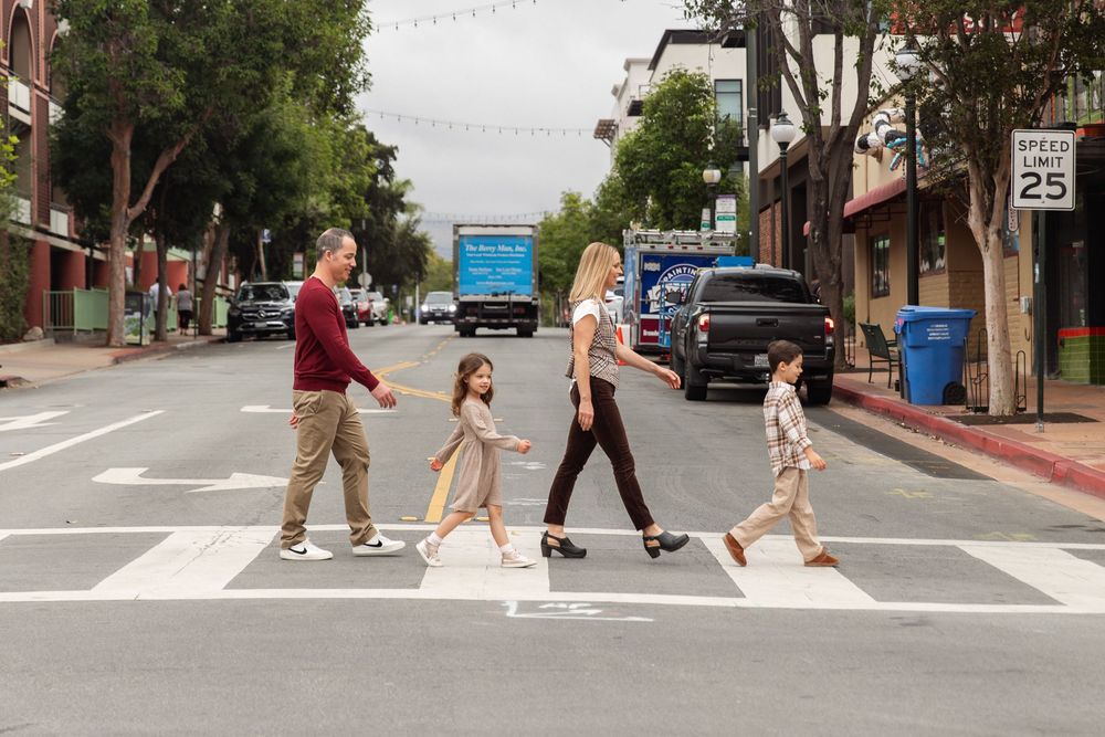 Family of four crossing a street crosswalk in a sunny town.