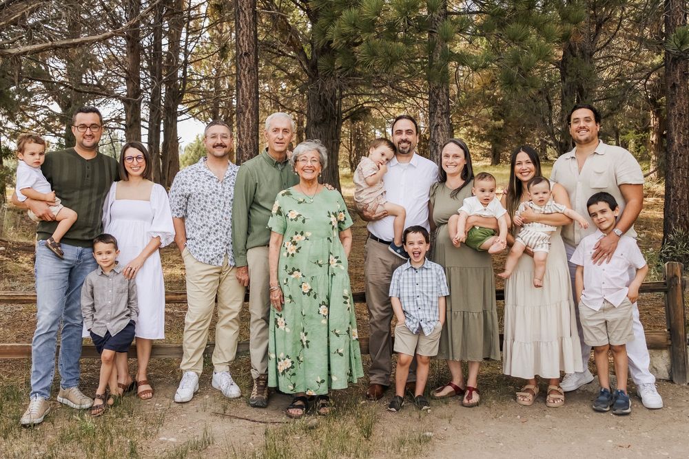 Large multigenerational family posing together outdoors among pine trees for a portrait photo.