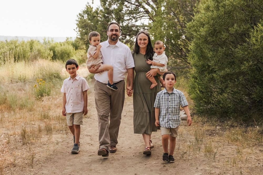 Family of six walks on a sandy trail surrounded by lush greenery during a warm outdoor photo session.