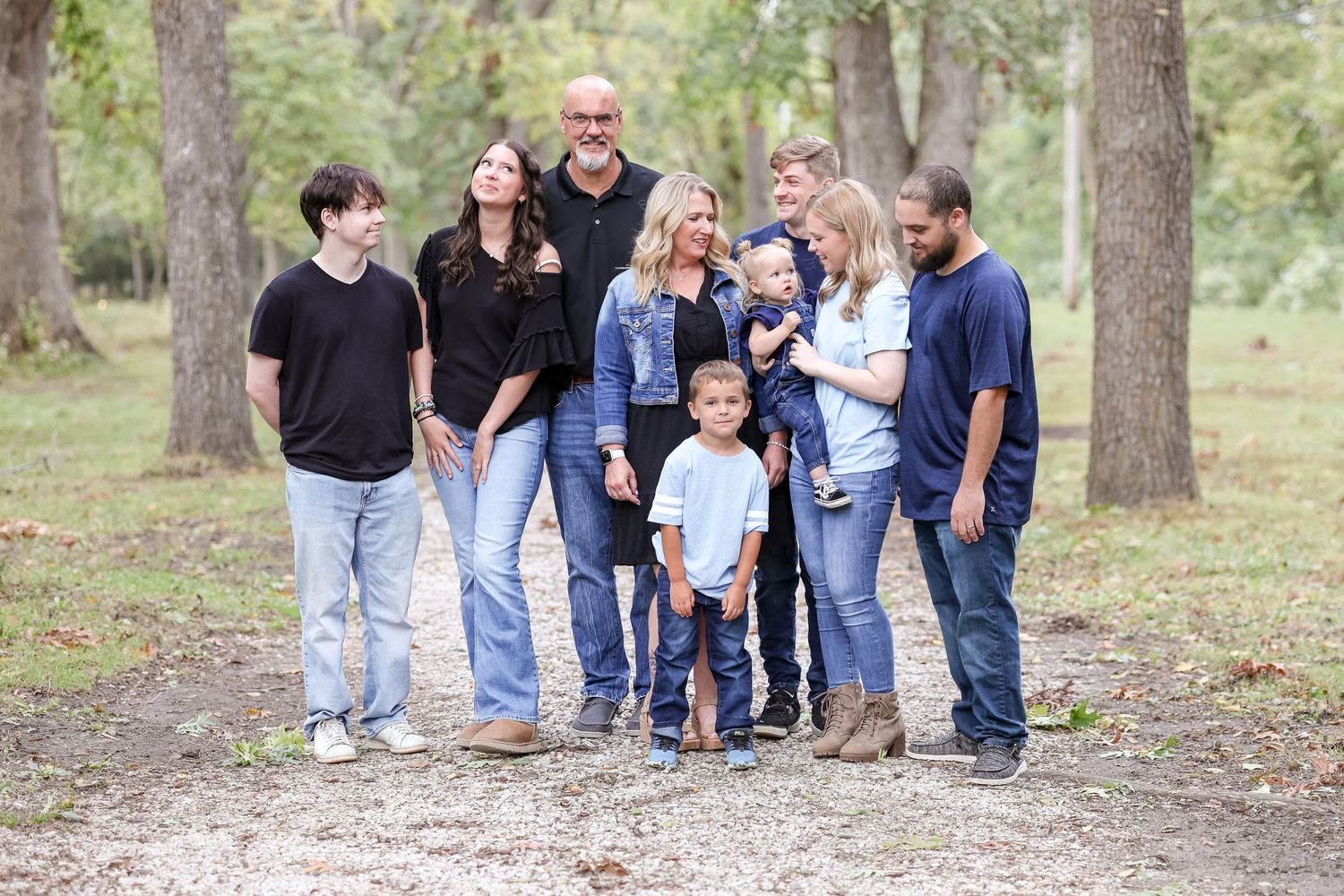 A casual family group stands together on a wooded path, wearing coordinated denim and casual clothing.