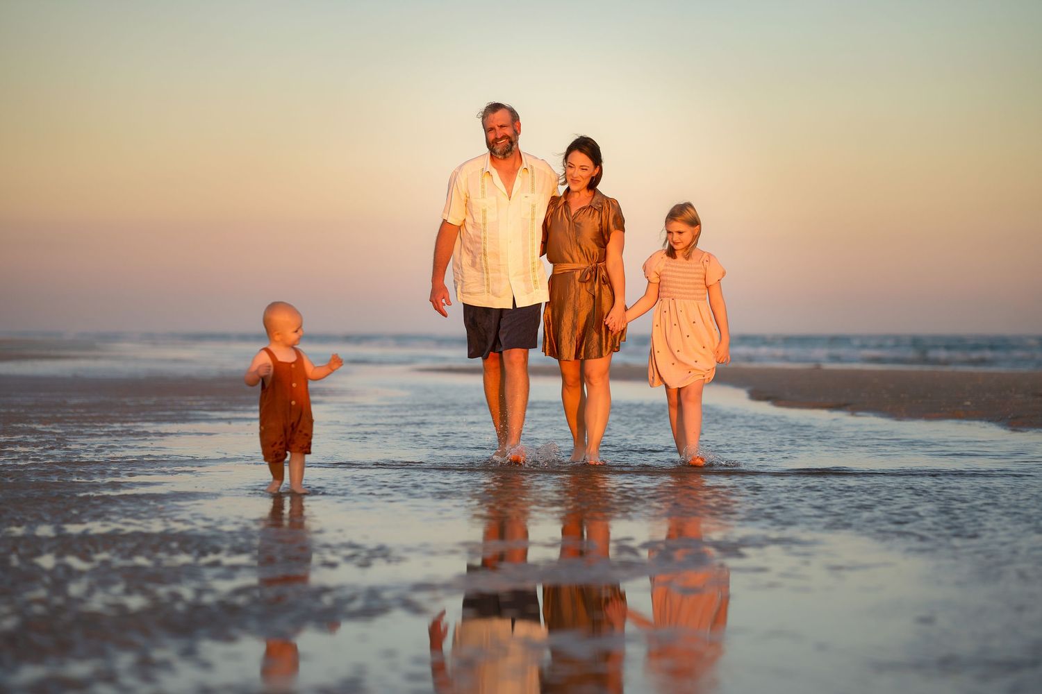 Matagorda Beach Family Photography. Family walks down beach with beautiful sunset behind them and strong reflection in puddles.