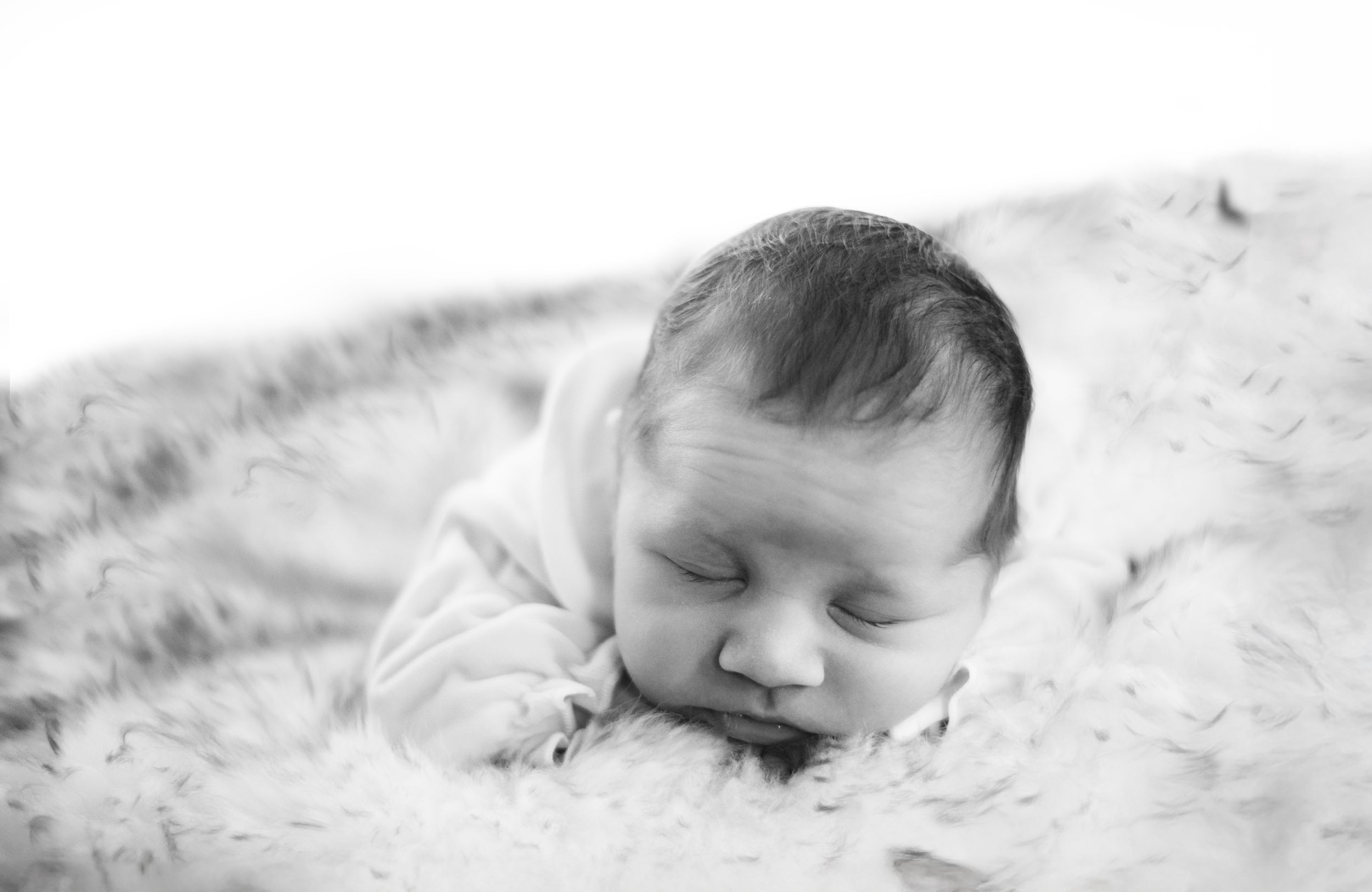 Sleeping baby in white clothing on textured white bedding.