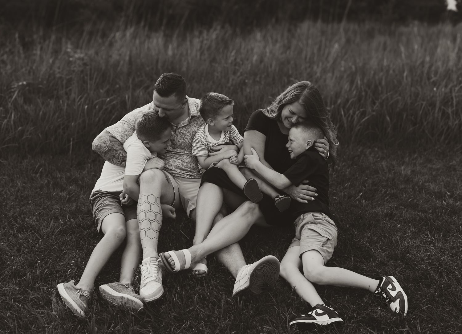 A playful black and white photo of a family lying together on grass. Colorado Springs Photographer.