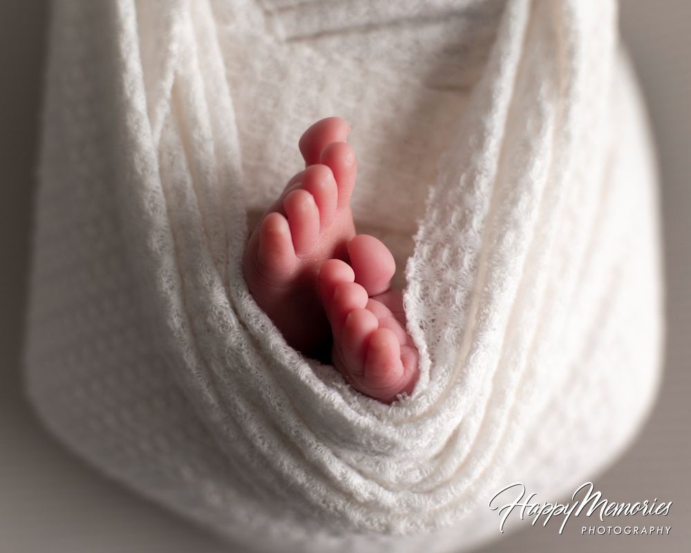 Tiny newborn baby feet peeking out from a soft cream knit wrap in a close-up newborn photography portrait.