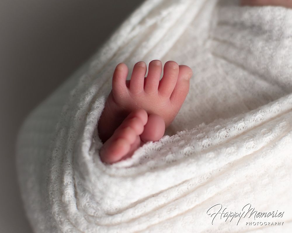 Close-up of a newborn baby's tiny feet peeking out from a soft cream knit wrap in a professional newborn photography portrait.