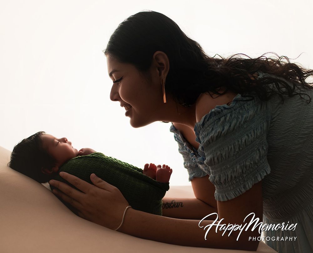 A mother tenderly gazes at her newborn baby wrapped in green, captured by Happy Memories Photography.