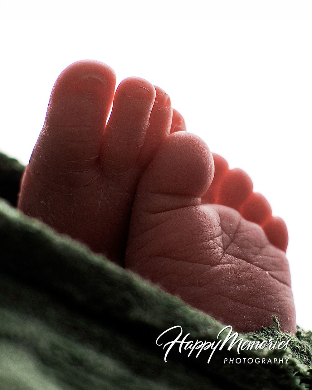 Close-up of tiny newborn baby feet resting on a soft green blanket, captured by Happy Memories Photography.