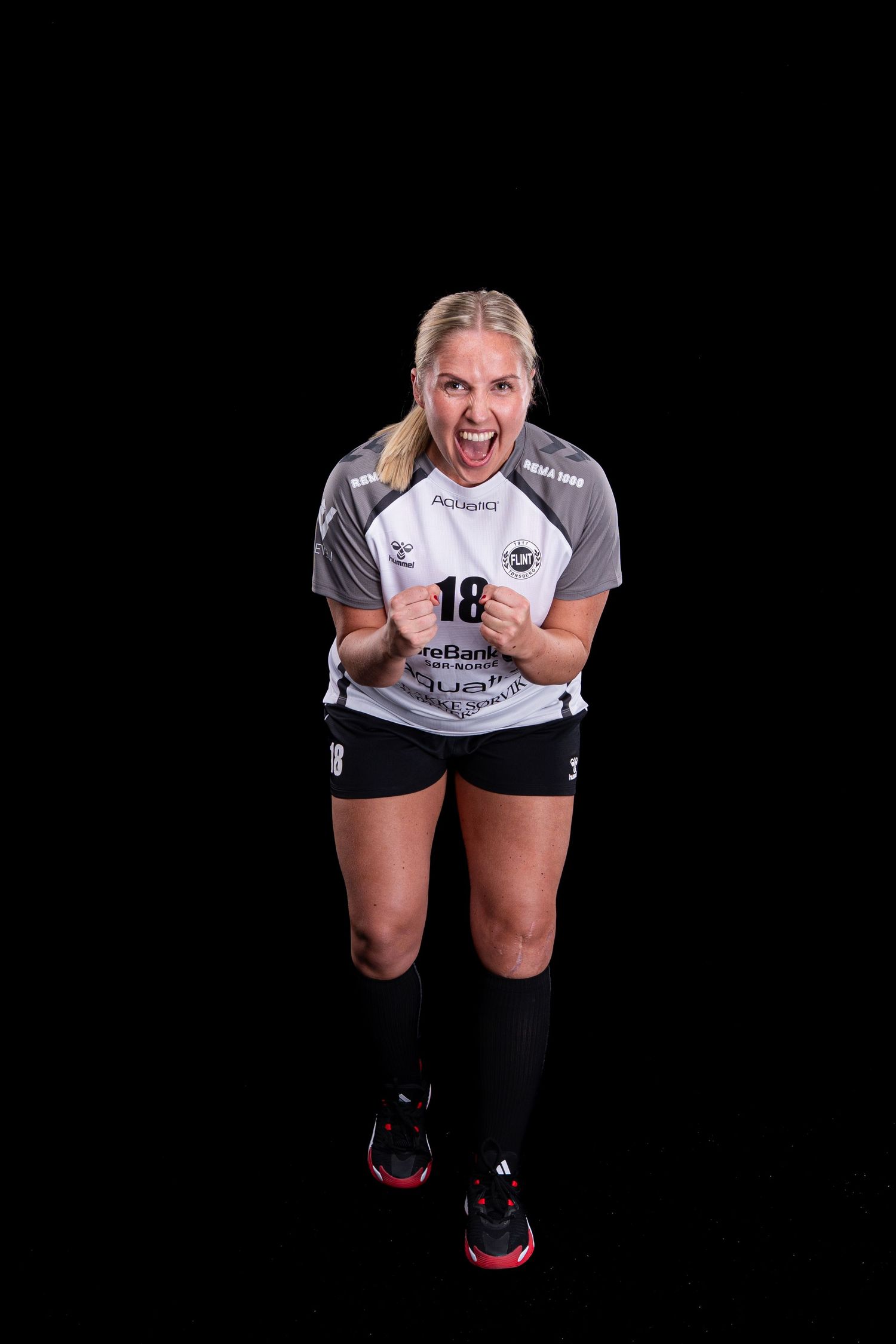 Athletic player in white jersey and black shorts shows intense emotion against dark background during sports photo shoot.