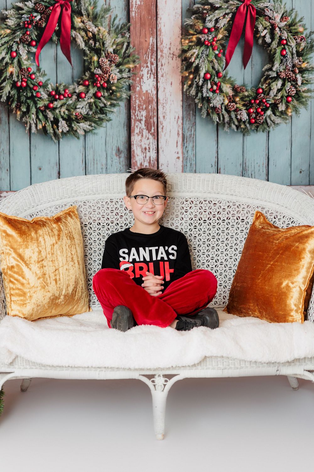 Holiday scene with Christmas wreaths on blue wood wall and white bench with velvet pillows decorated for winter. studio session clayton, nj