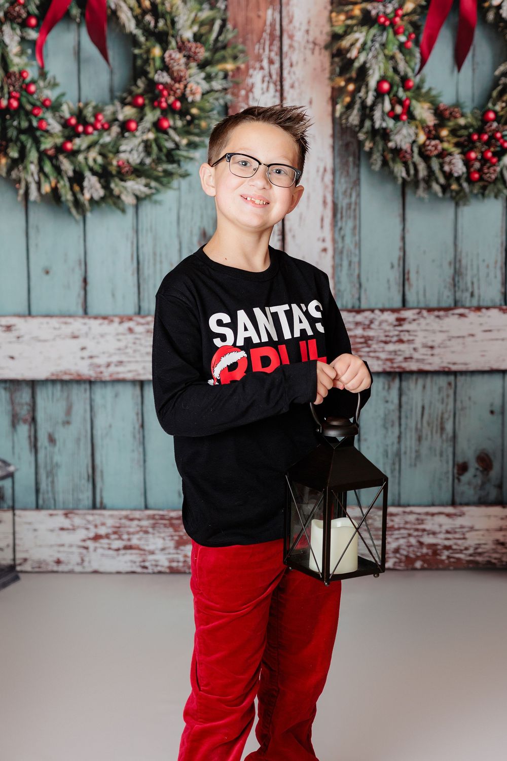 Red and silver Christmas photoshoot setup with rustic wooden backdrop, wreaths, lanterns, and festive decor. studio session clayton nj