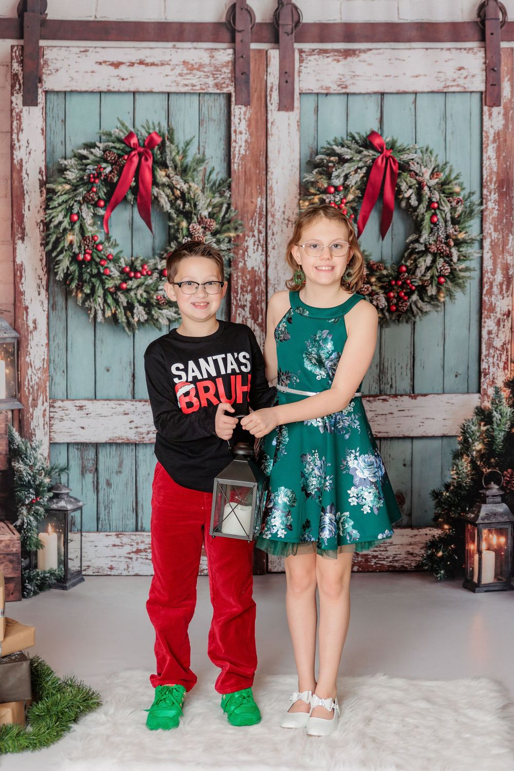 Children in festive holiday outfits pose against rustic backdrop with Christmas wreaths and turquoise doors. studio session clayton nj