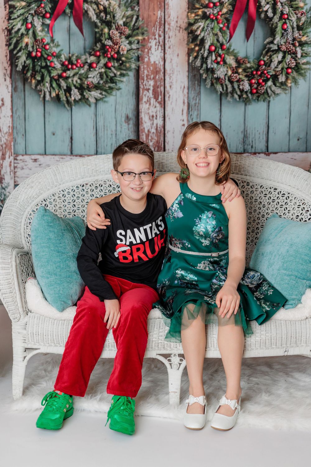 Four similar photos of siblings sitting on a wicker bench against a blue wall decorated with Christmas wreaths. studio session clayton nj