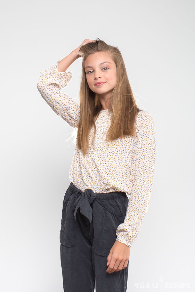 Portrait against white background showing casual style with polka dot blouse and dark pants.