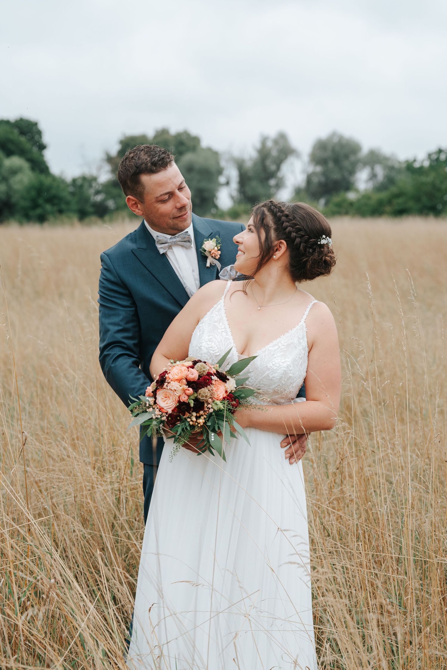 A couple in wedding attire embraces in a golden wheat field during their romantic outdoor photography session.