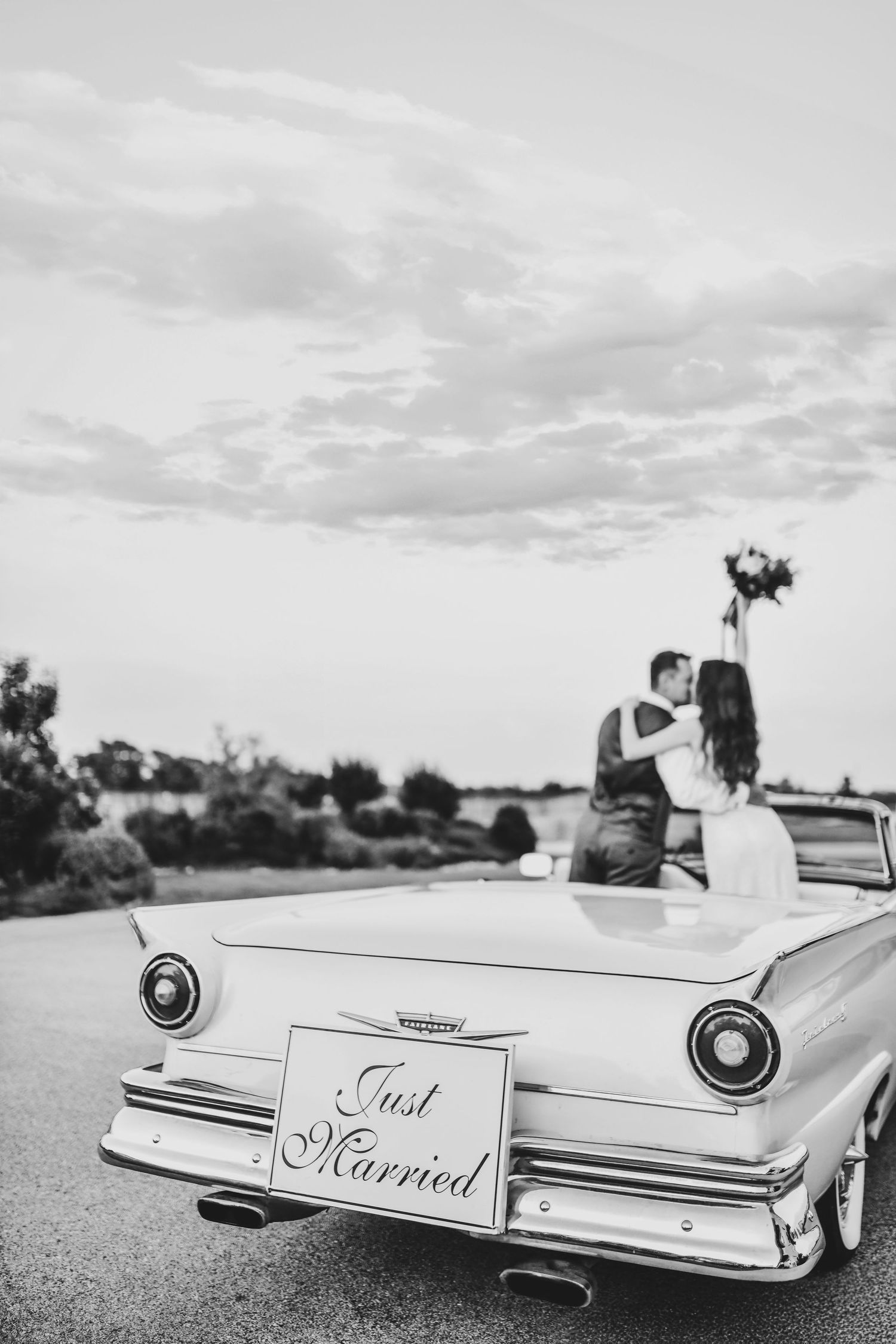 editorial black and white photo of bride and groom kiss as they drive off after their wedding at oak and ivy