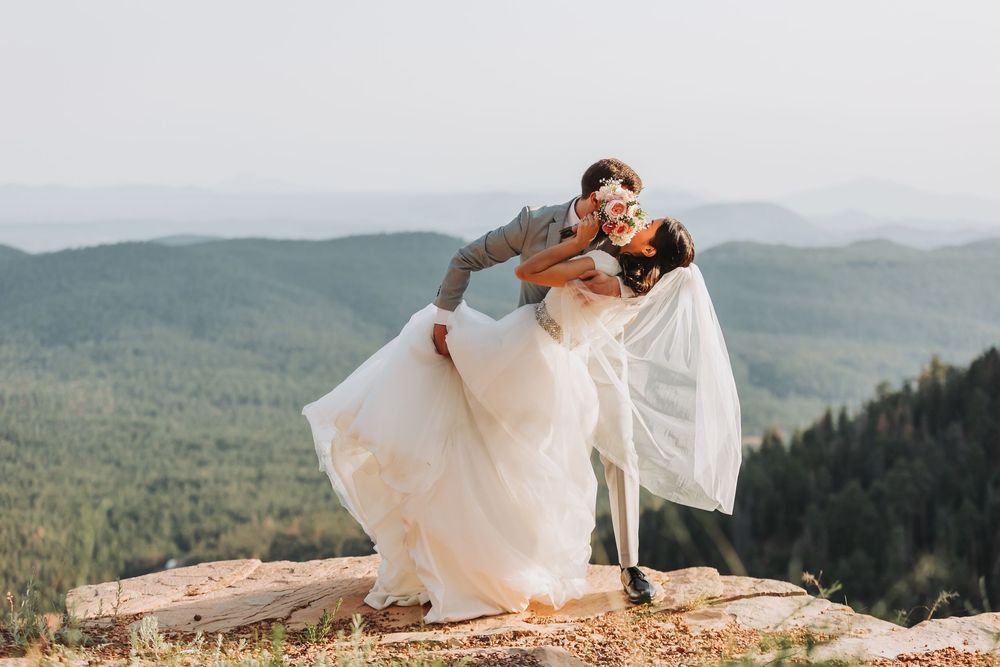 A scenic mountaintop photo session with flowing white dress fabric against a backdrop of rolling hills and forests.