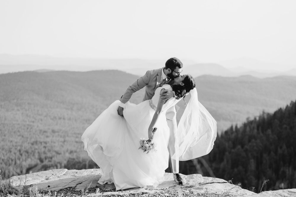 Black and white wedding photo featuring a flowing white dress against a mountainous backdrop.