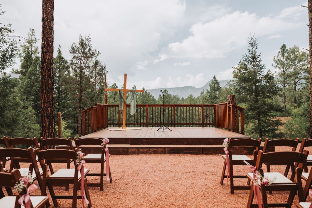 Wide-angle panorama of a rustic outdoor wedding venue with wooden benches and mountain vistas in the background.