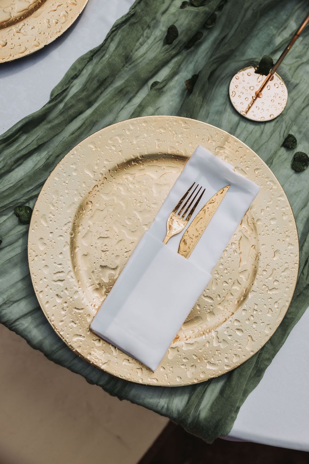 Close-up details of elegant place settings with cream-colored plates, gray napkins, and metallic utensils on green linens.